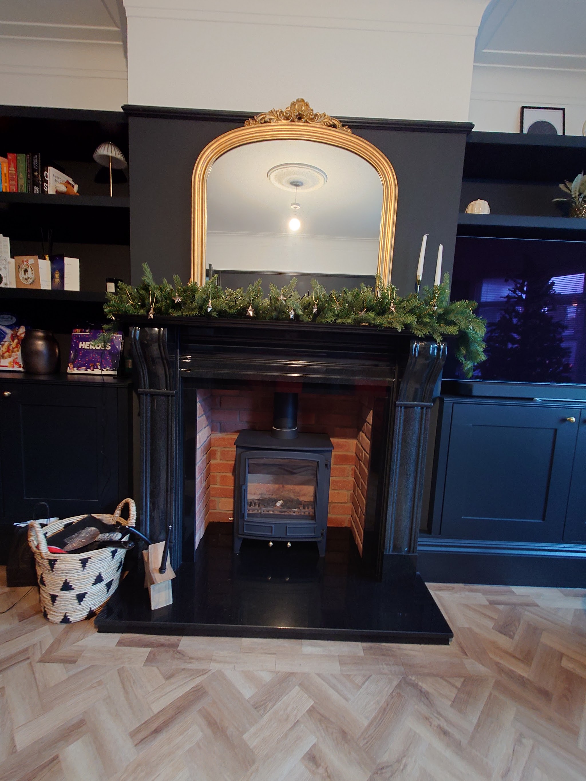 A black multi-fuel stove in a black fireplace surround with a gold mirror and garland above