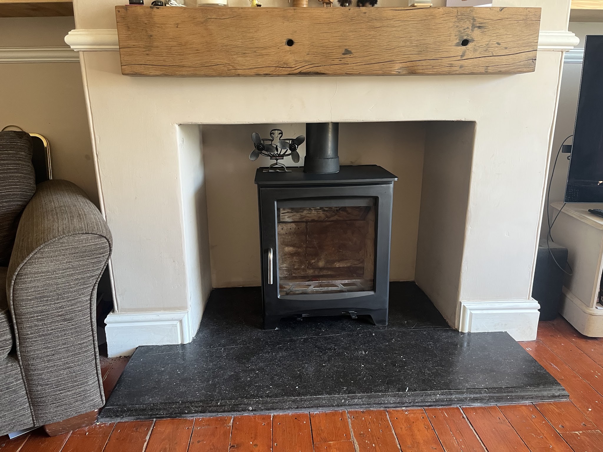 The same wood burner afterwards, clean, in a cream surround under an oak beam